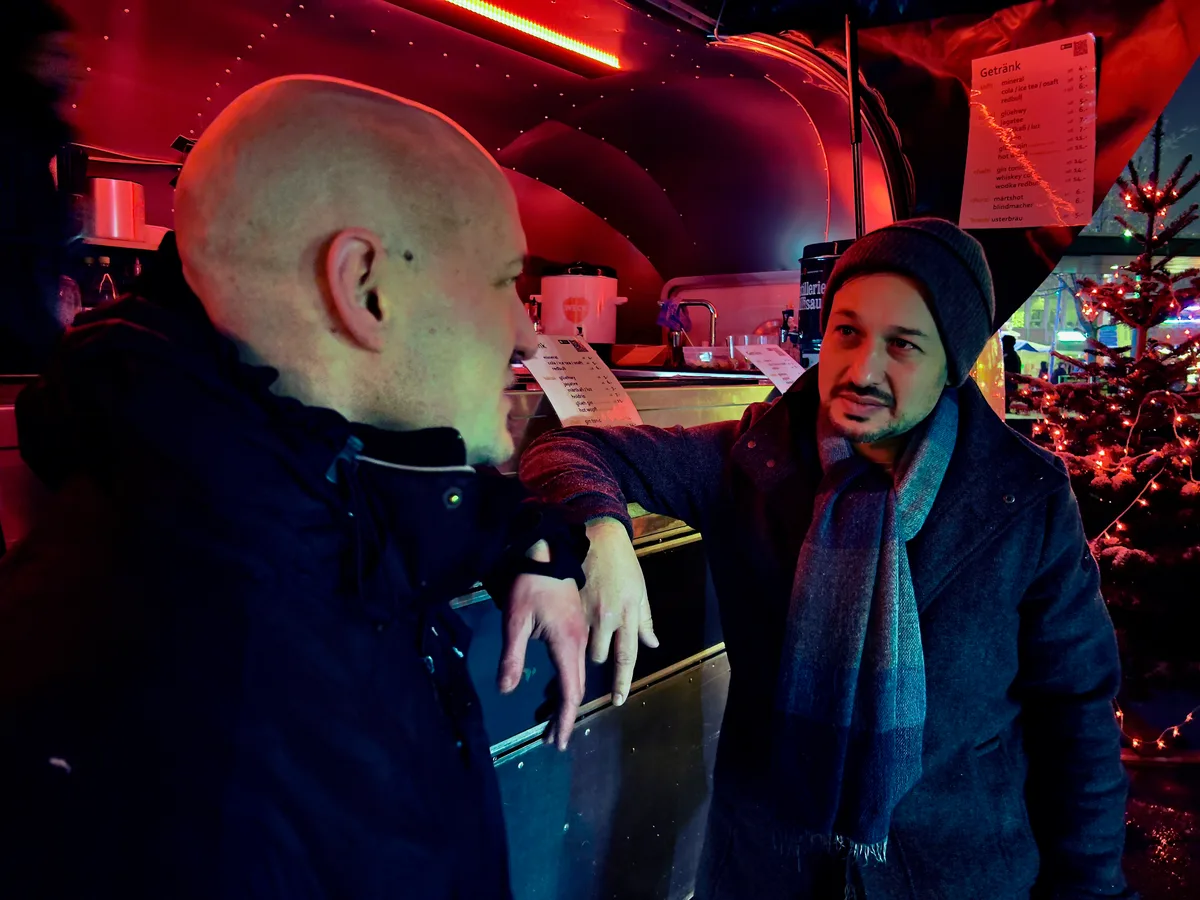 Man sieht zwei Männer im Gespräch, angelehnt an die Theke eines Foodtrucks.